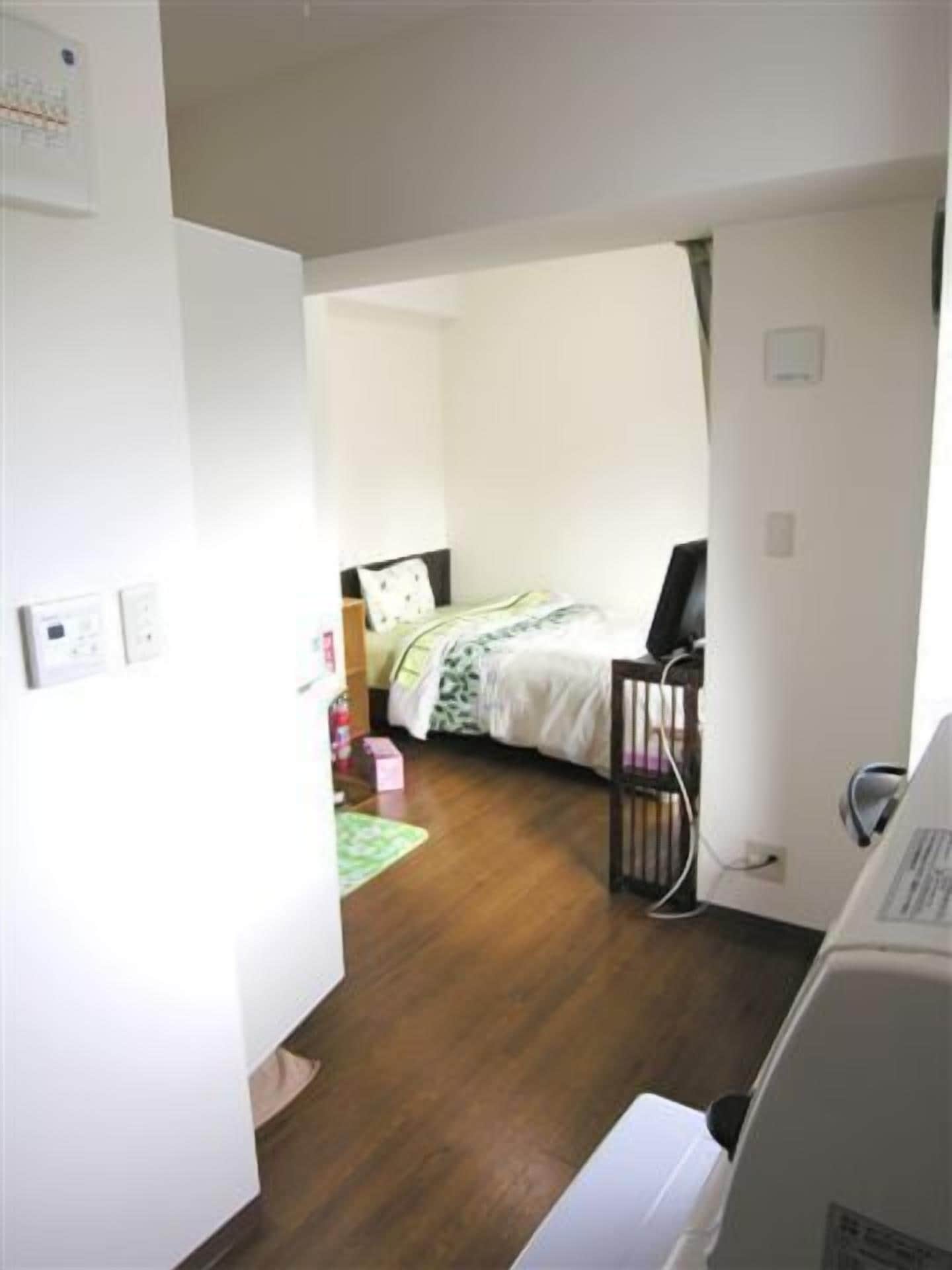 Een kamer met een bed, een bureau en een stoel. Er is een raam met gordijnen, een deur en een airconditioner aan de muur.