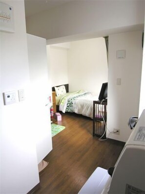 Ein Zimmer mit einem Bett, einem Schreibtisch und einem Stuhl. Es gibt ein Fenster mit Vorhängen, eine Tür und eine Wand-Klimaanlage.