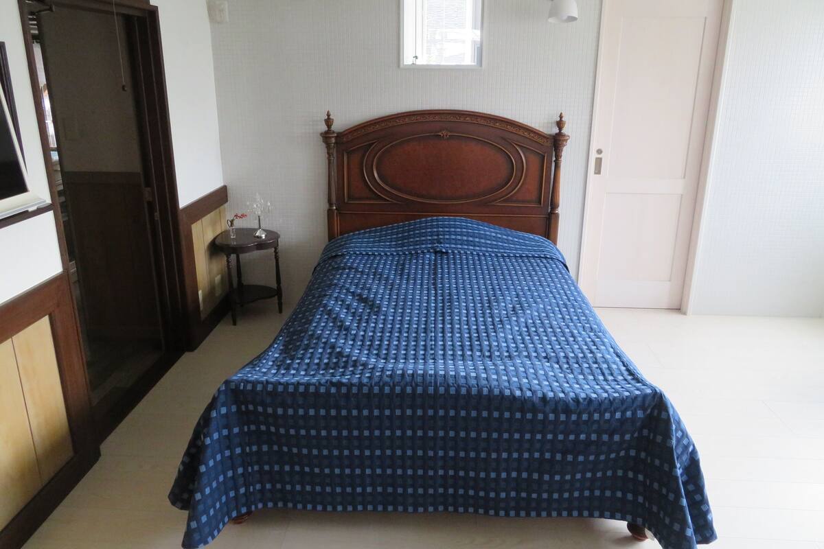 A bedroom with a wooden bed, a small bedside table, a window with a view, and a door.
