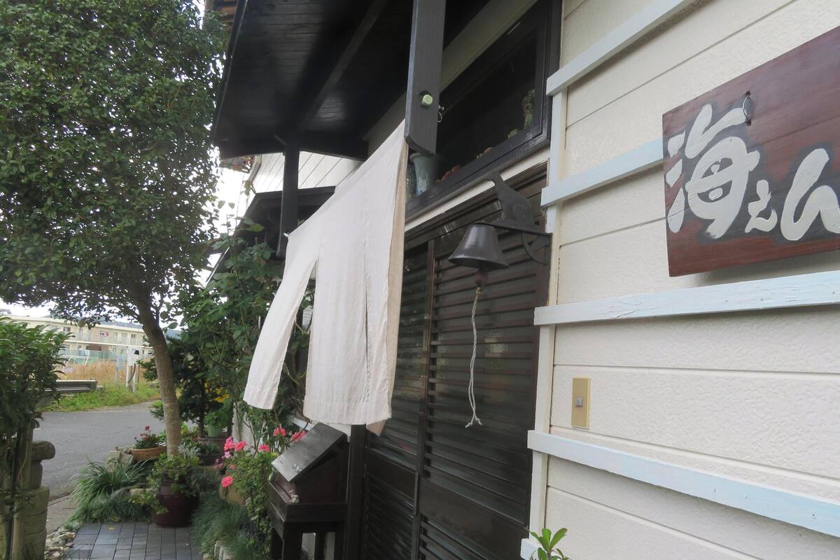 A building with a closed shutter, a hanging bell, and a sign with Japanese characters.