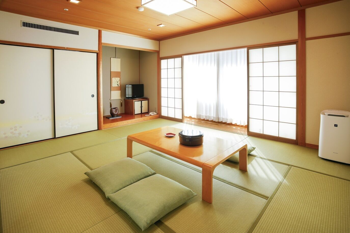A traditional Japanese room with tatami flooring, a low wooden table, cushions, sliding doors, a television, and a heater.