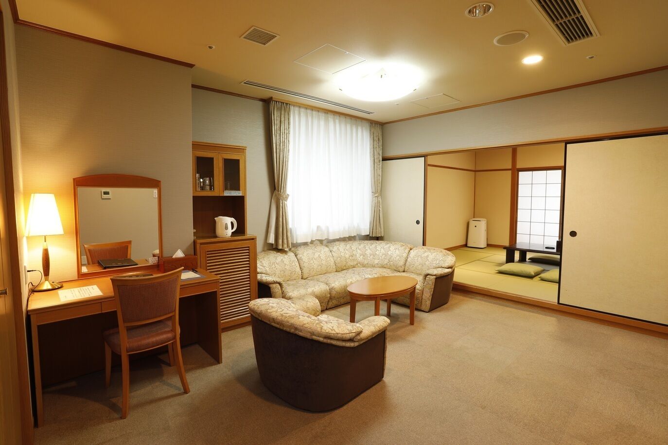 A hotel room with a sofa, armchair, desk, and cabinet.