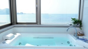 Un baño con bañera, una ventana con vistas al mar y una planta en el alféizar.
