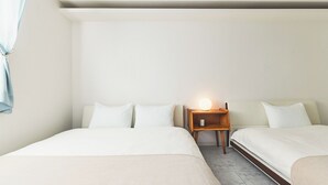 Una habitación de hotel con dos camas, una mesita de noche con lámpara y una ventana con cortinas.