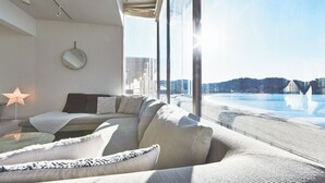 Una sala de estar moderna con un sofá, una lámpara de pie con forma de estrella, un espejo redondo y vistas a una playa a través de amplios ventanales.