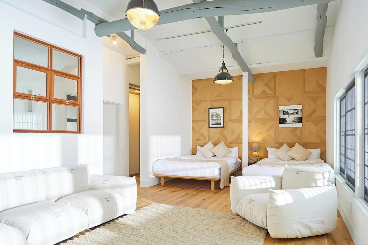 Un dormitorio moderno con dos camas, un sofá blanco, suelo de madera y un ventanal grande.