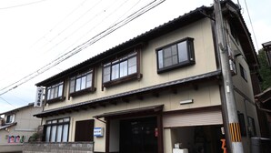 Un edificio a due piani con uno stile architettonico tradizionale, caratterizzato da un'ampia entrata con porta scorrevole, un piccolo portico e un cartello ben visibile.
