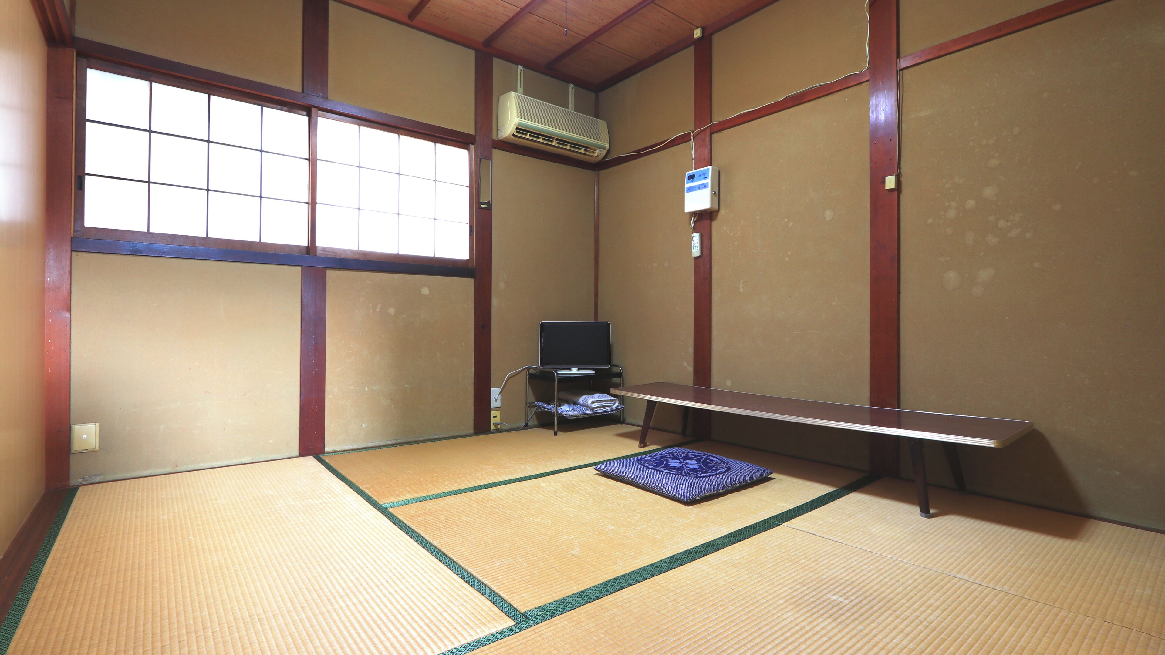 Ein Zimmer mit Tatami-Matten, einem Fernseher, einer Klimaanlage und einer Bank.
