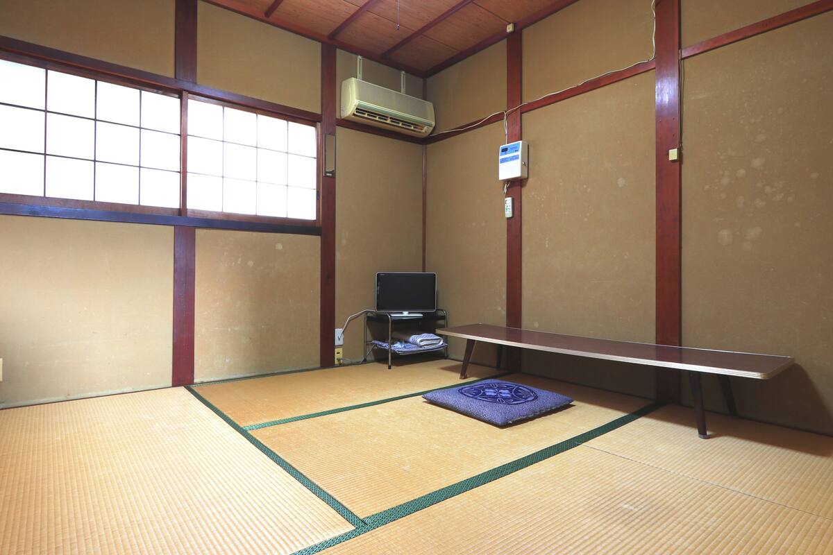 Una habitación con esterillas de tatami, televisor, aire acondicionado y un banco.