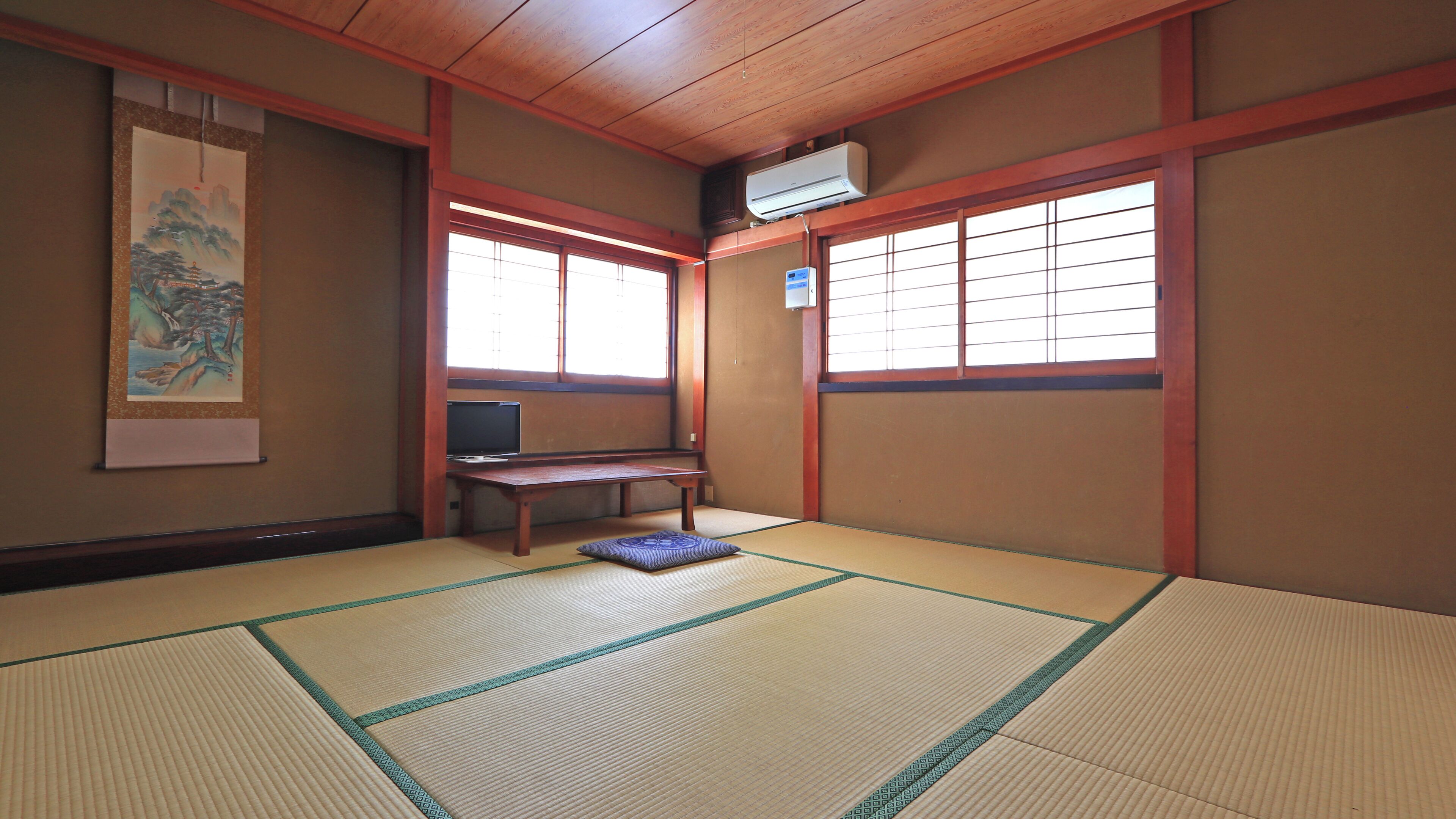 Ein traditioneller japanischer Raum mit Tatami-Boden, einem Fernseher und einem Gemälde an der Wand.