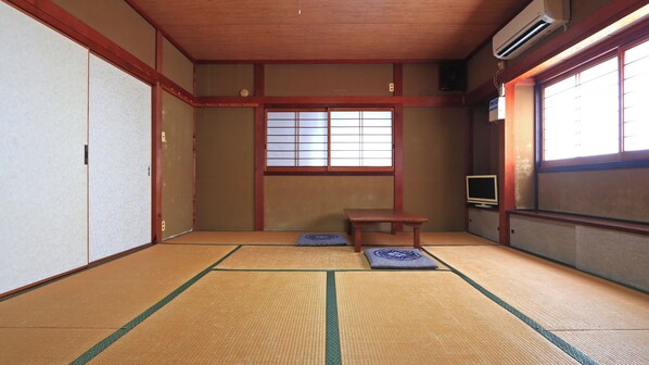 Una habitación tradicional japonesa con suelo de tatami, puerta corredera, ventana con paneles shoji, un televisor y una mesita.