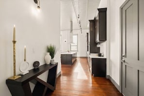 A hallway with a wooden floor, a dark console table with a vase and a clock, and a door on the right. - Luxury Penthouse | Rooftop Deck Best Street in OTR (Cincinnati)