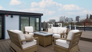 Una terraza en la azotea con mobiliario de mimbre, una mesa central y vistas al horizonte de la ciudad.