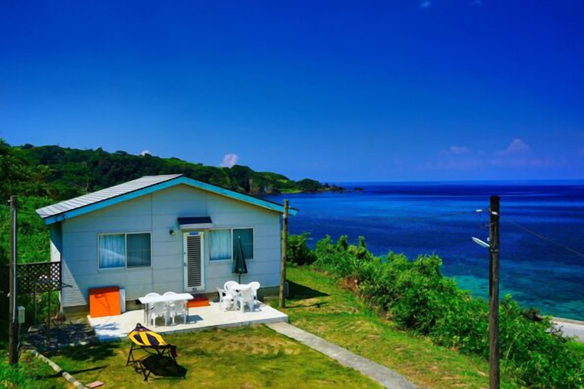 Una pequeña casa con techo azul, paredes blancas y un patio con mobiliario exterior.