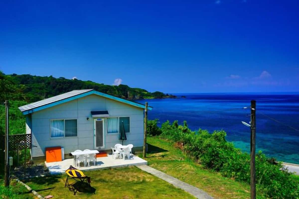 A small house with a blue roof, white walls, and a patio with outdoor furniture.