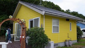 A yellow house with a porch, a small garden, and propane tanks outside. - Sado Seaside Villa (Sado)