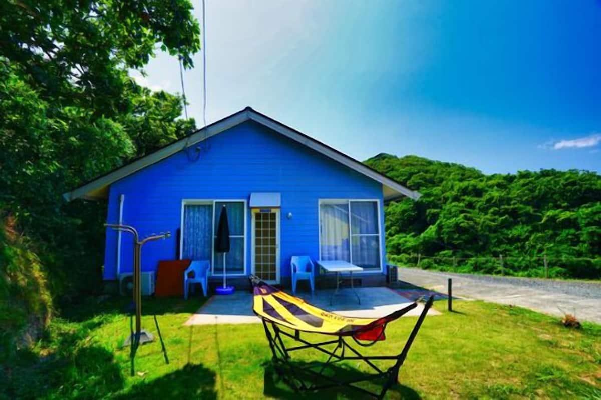 A blue house with a porch, a hammock, and a small table.
