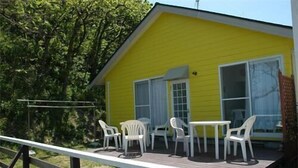 A yellow building with a deck, white chairs, and a table. - Sado Seaside Villa (Sado)