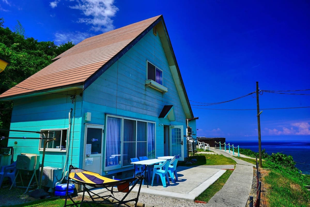 A blue house with a red roof, a small window, and a table with chairs outside.