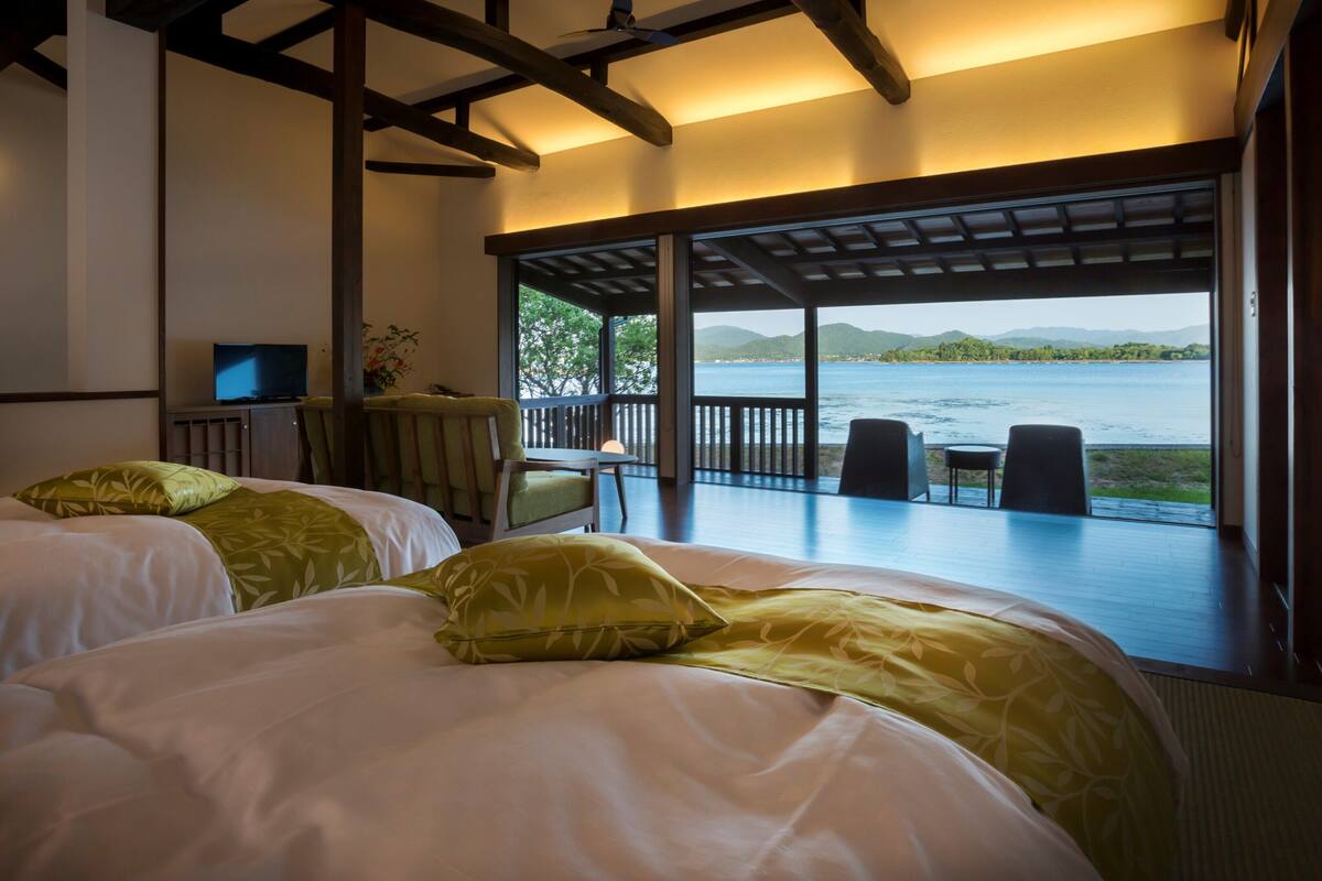 A room with two beds, a TV, and a balcony with a view of the water.