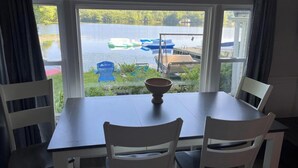 Une table à manger avec deux chaises, un bol, et une vue sur des bateaux sur un lac, visible par une fenêtre.
