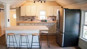 Une cuisine dotée d’un îlot central, de tabourets de bar, d’un réfrigérateur et d’une porte coulissante.