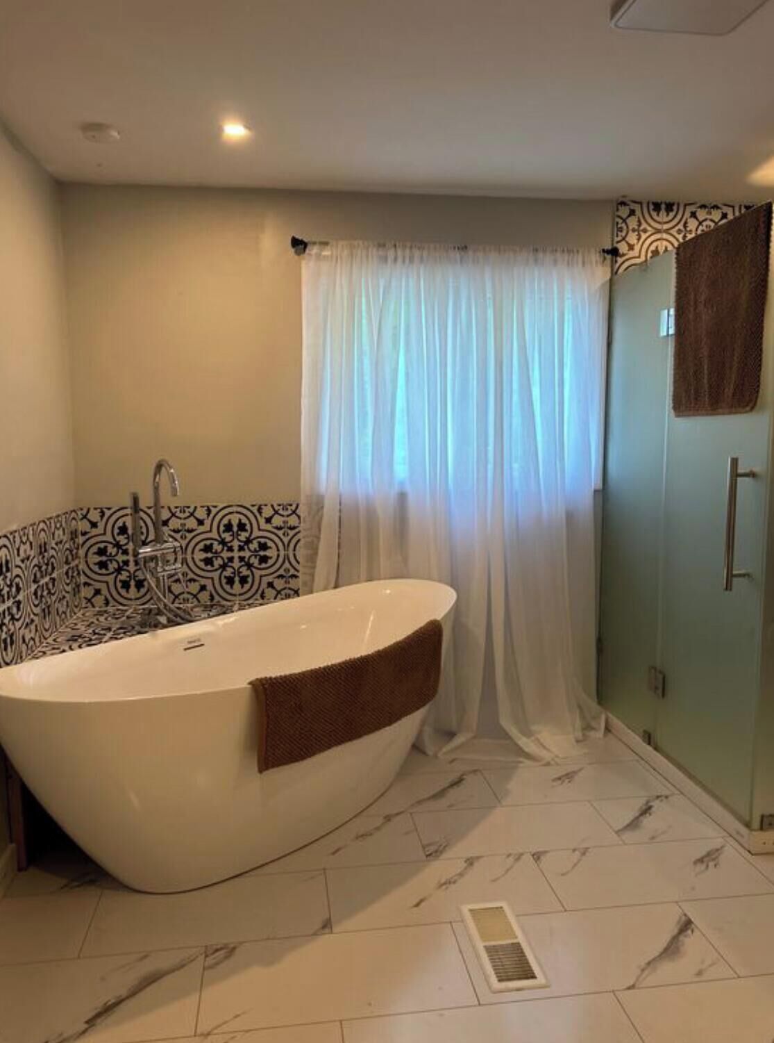 A bathroom with a freestanding bathtub, patterned tiles, a shower curtain, and a towel.