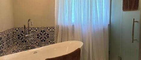 A bathroom with a freestanding bathtub, patterned tiles, a shower curtain, and a towel.