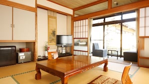 Una tradizionale stanza giapponese con pavimenti in tatami, un tavolo di legno, un televisore e porte scorrevoli che danno su uno spazio esterno.