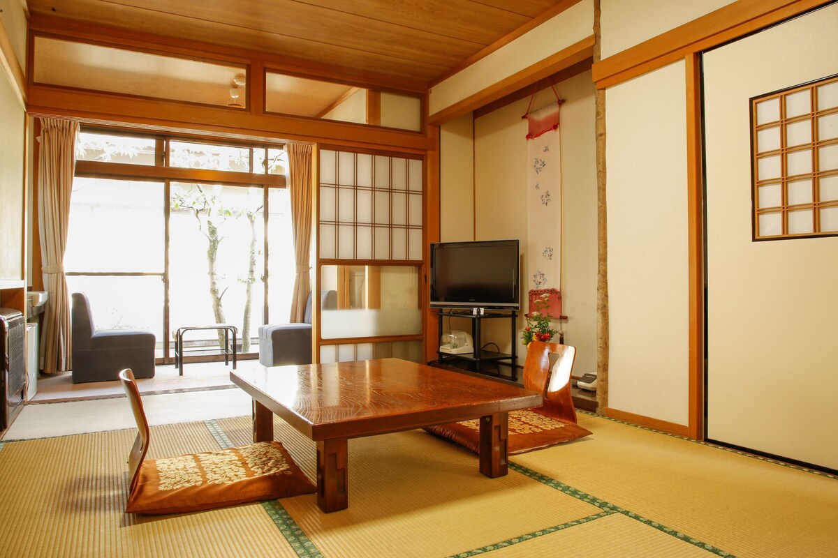 A traditional Japanese room with tatami flooring, a low table, a television, and sliding doors.