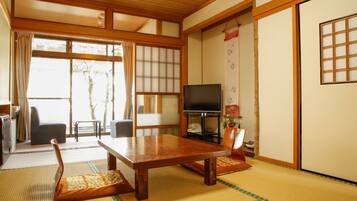 A traditional Japanese room with tatami flooring, a low table, a television, and sliding doors.