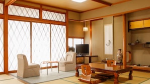 Una tradizionale stanza giapponese con pavimento in tatami, un tavolino, sedie, un televisore e un vaso decorativo.