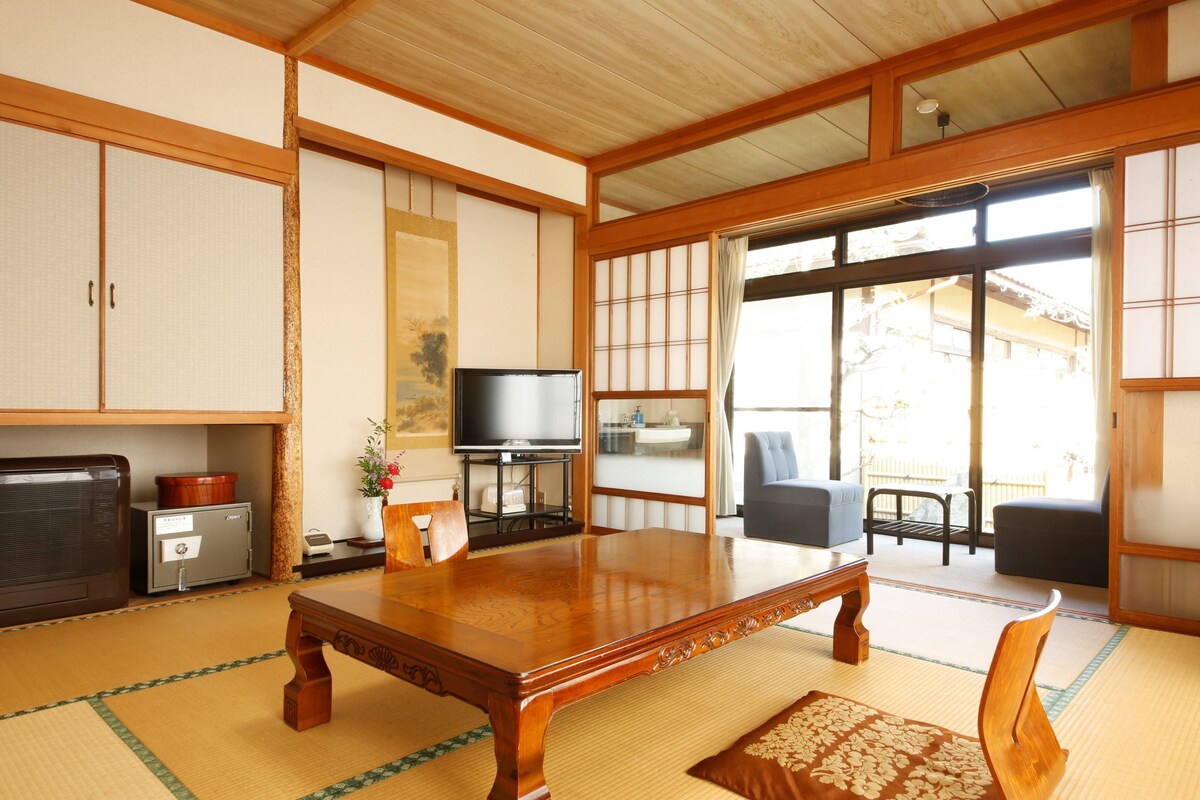 A traditional Japanese room with tatami flooring, a wooden table, a television, and sliding doors leading to an outdoor area.