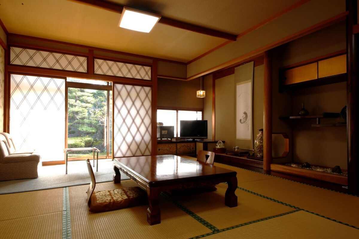A traditional Japanese room with tatami flooring, a low table, a television, and sliding doors.