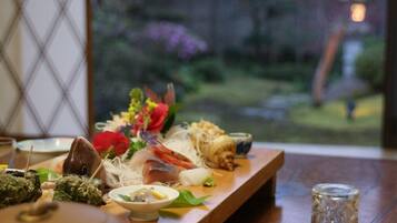 A wooden table with various seafood dishes and a small bowl of soup, set against a window with a view of greenery.