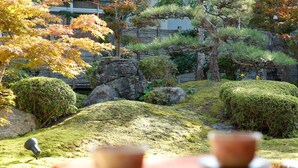 Un giardino giapponese tradizionale con una lanterna in pietra, un piccolo stagno e due tazze su un tavolo.
