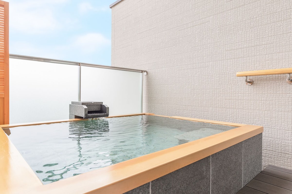 A hot tub with a wooden frame, a stone wall, and a wooden panel on the left.