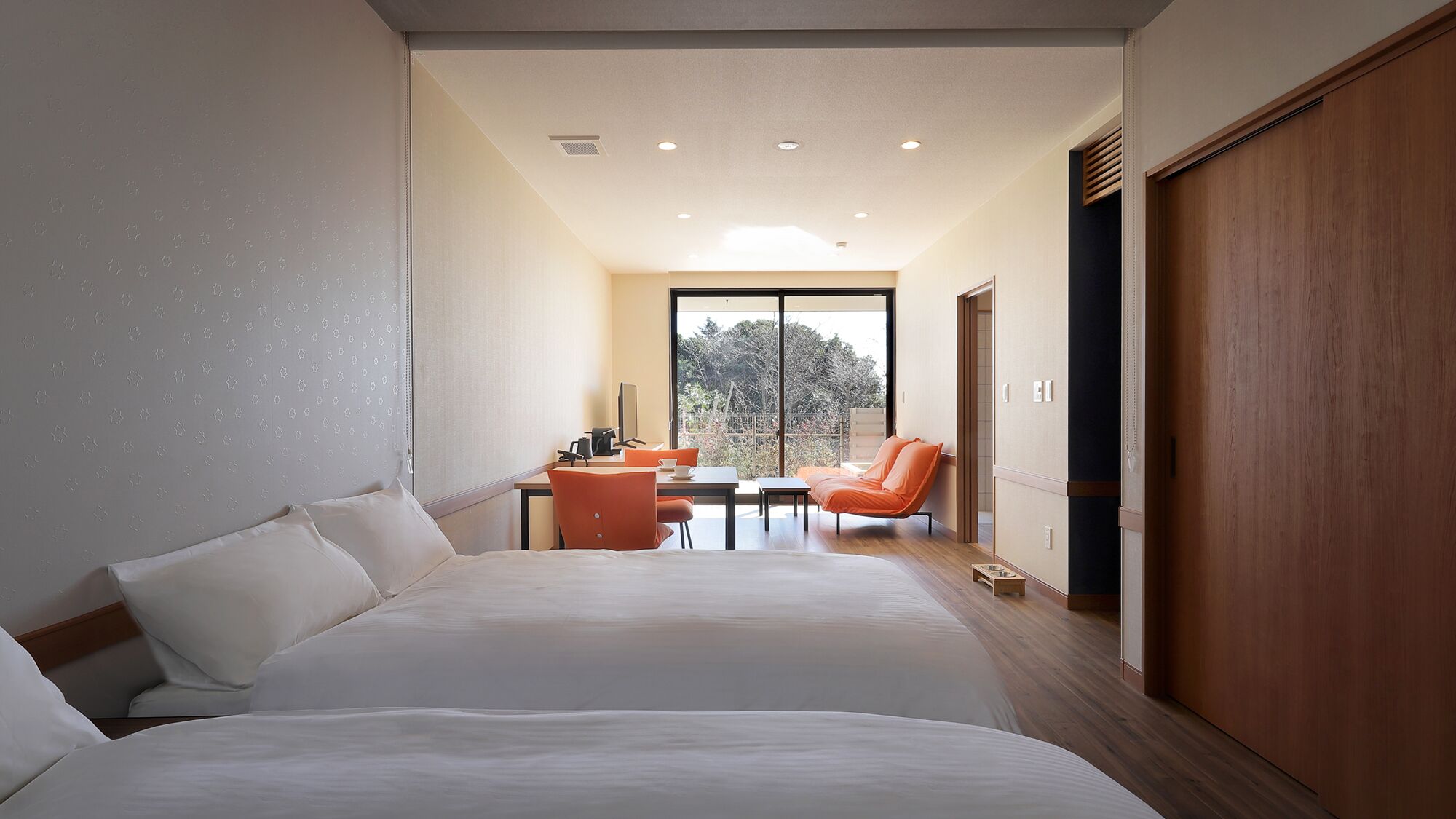 A hotel room with a large bed, a desk with a chair, a small table, and a view through a large window.