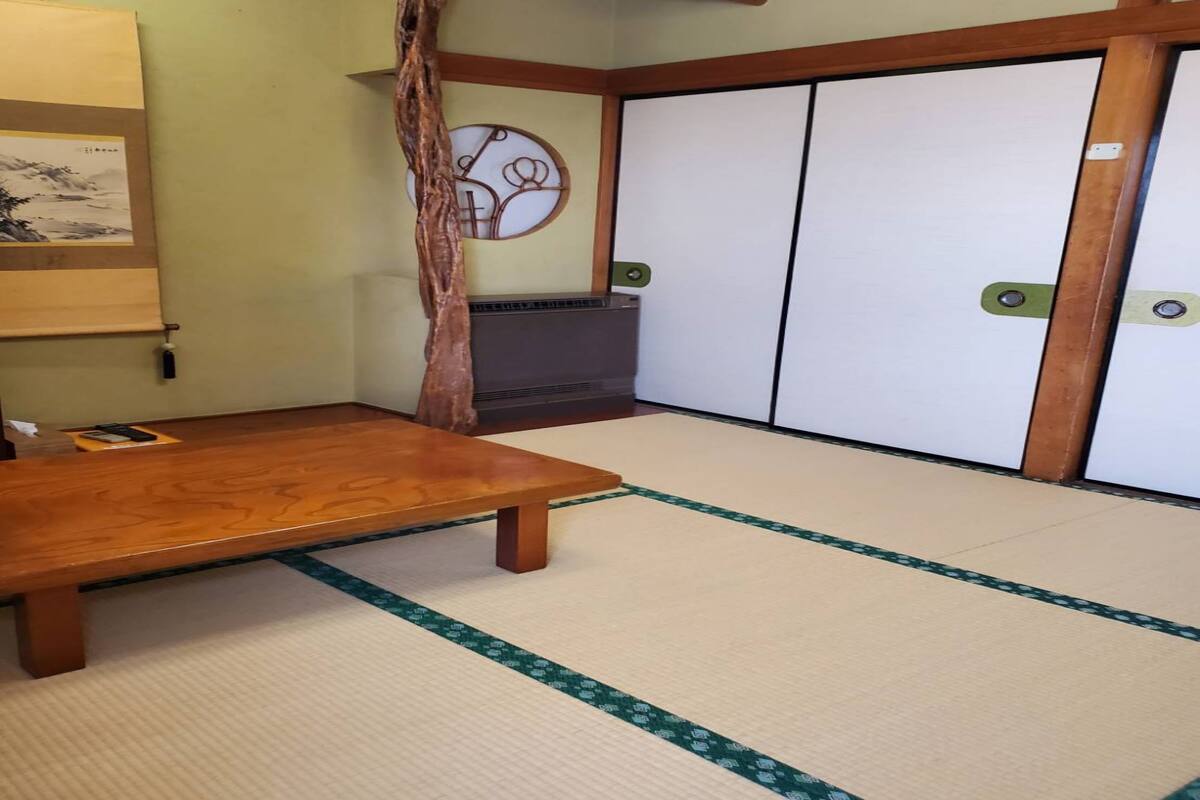 A traditional Japanese room with tatami flooring, a low wooden table, sliding shoji doors, and a hanging wooden decoration.