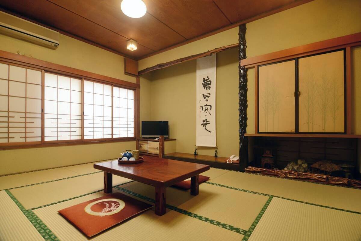 A traditional Japanese room with tatami flooring, a low table, a television, and sliding doors.