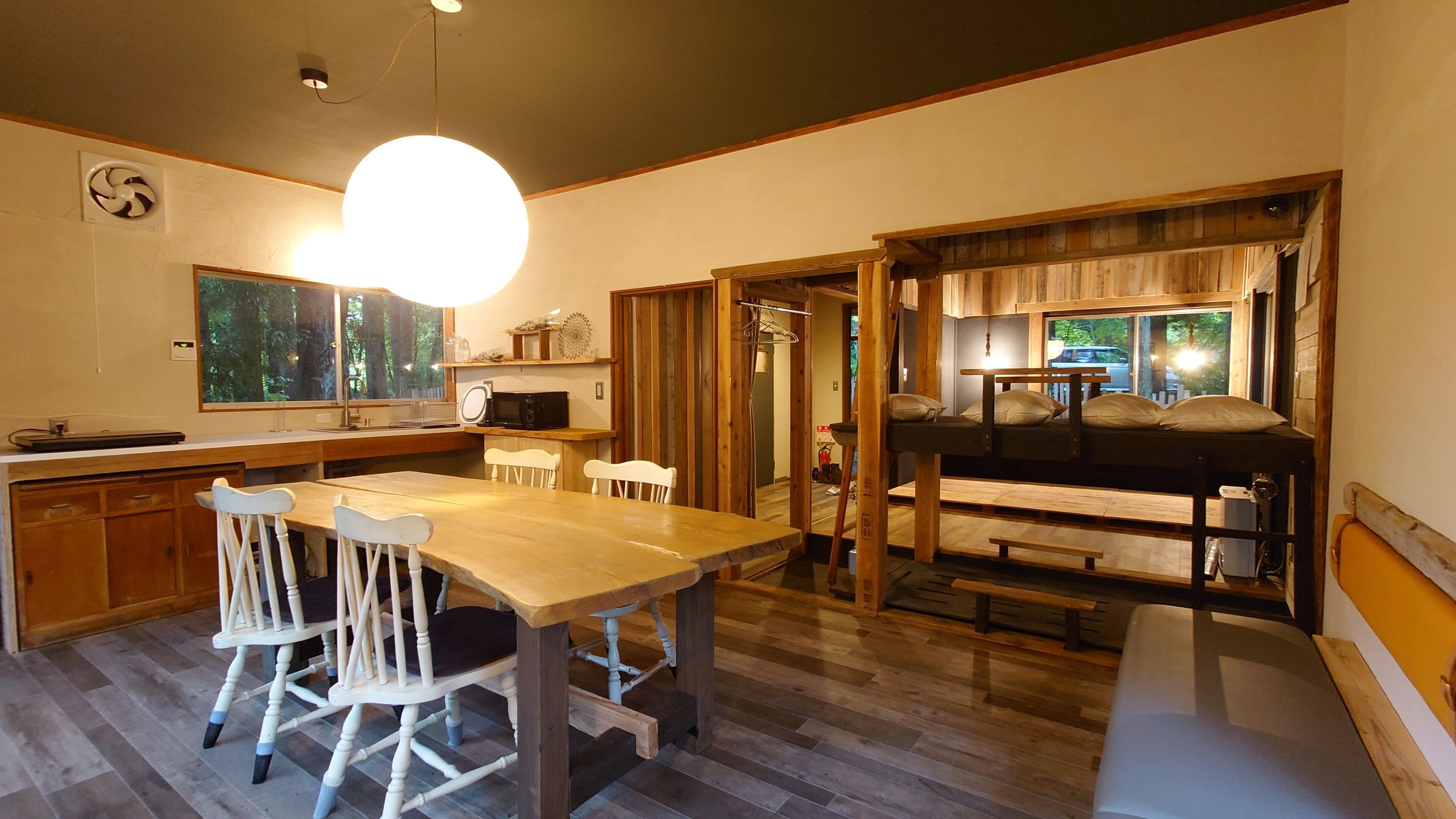 A cozy kitchen with wooden cabinets, a dining table with chairs, a hanging light fixture, and a view through a window.