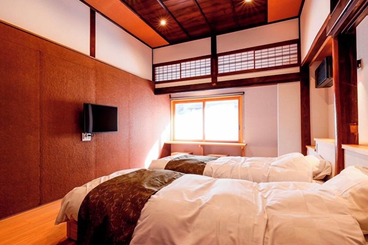A room with two beds, a TV on the wall, and a window with a view.
