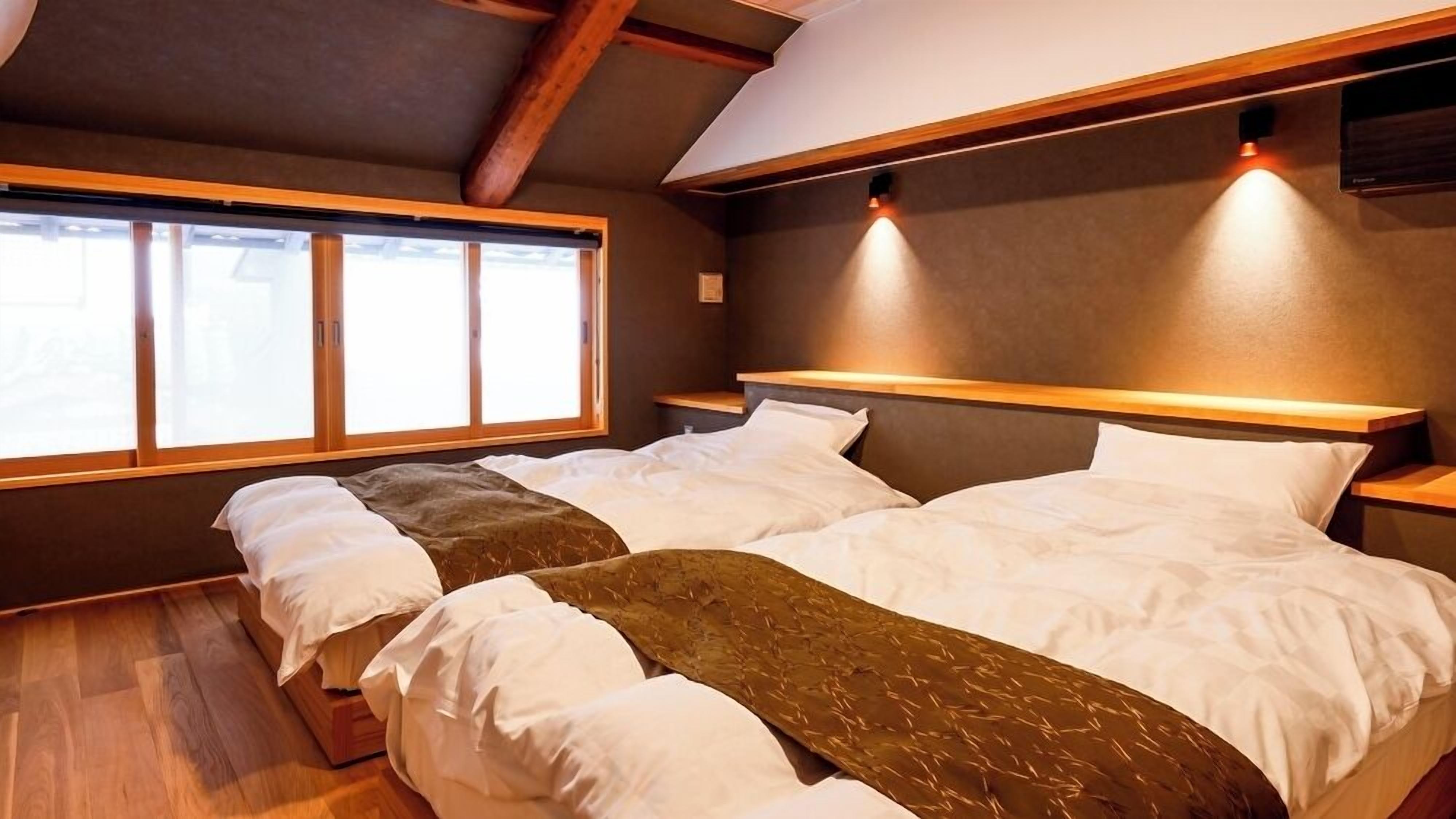 Una habitación con dos camas, vigas de madera, una ventana y una lámpara fijada a la pared.