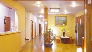 A hotel corridor with a reception desk, a potted plant, a painting on the wall, and a refrigerator. - Kusatsu Onsen Ryokan Yakumo (Kusatsu)