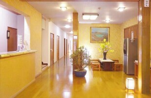 Un pasillo de hotel con mostrador de recepción, una planta en maceta, un cuadro en la pared y un refrigerador.