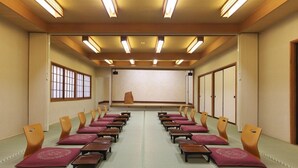A conference room with rows of chairs, a stage, and wooden paneling. - Kusatsu Onsen Ryokan Yakumo (Kusatsu)
