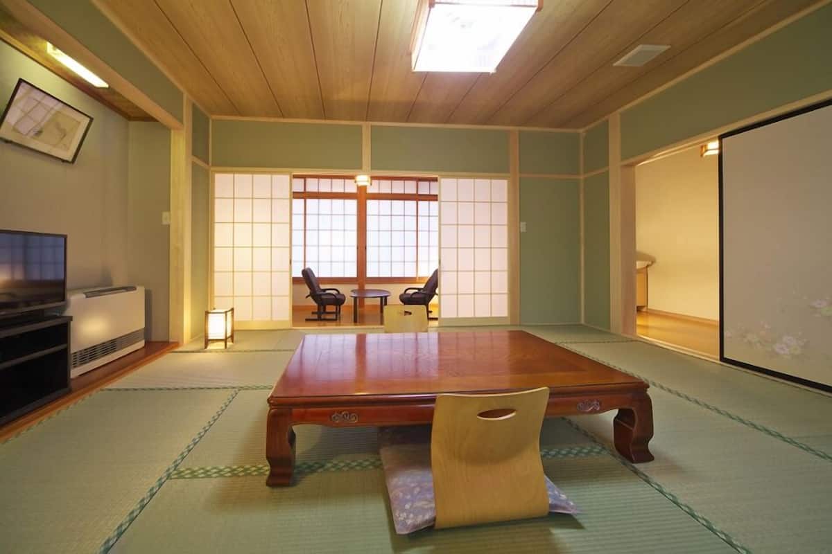 Una habitación japonesa tradicional con suelo de tatami, una mesa de madera baja, dos sillas, un televisor y una puerta corredera.