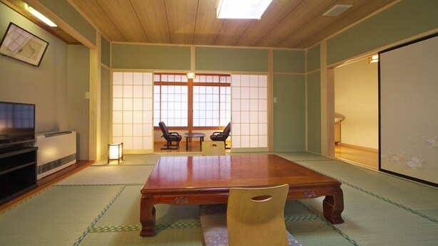 A traditional Japanese room with tatami flooring, a low wooden table, two chairs, a television, and a sliding door. - Kusatsu Onsen Ryokan Yakumo (Kusatsu)