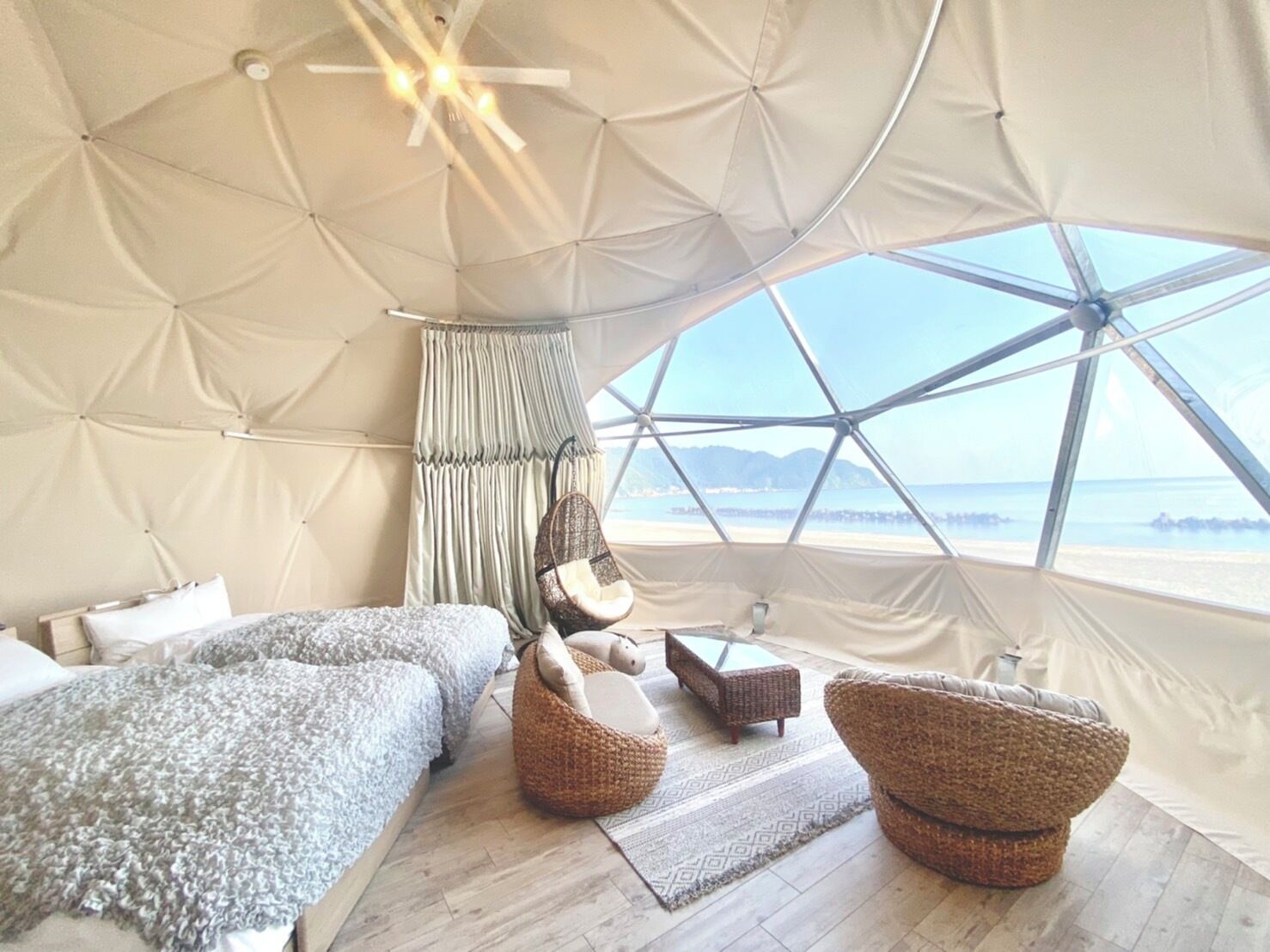 A tented accommodation with a bed, seating area, and a view of the sea.
