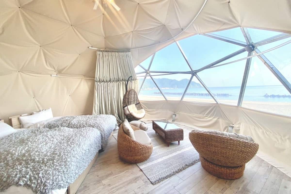 A tented accommodation with a bed, seating area, and a view of the sea.